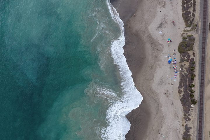 A bird’s eye view of San Clemente State Beach in Southern California shows Pacific Ocean waves lapping onto shore, a cluster of umbrellas and, to the far right, a rail corridor that serves passenger and freight trains. UC Irvine’s Brett Sanders says San Clemente is one of many examples of beaches in California that demonstrate their value in multiple ways. UC Irvine Flood Lab