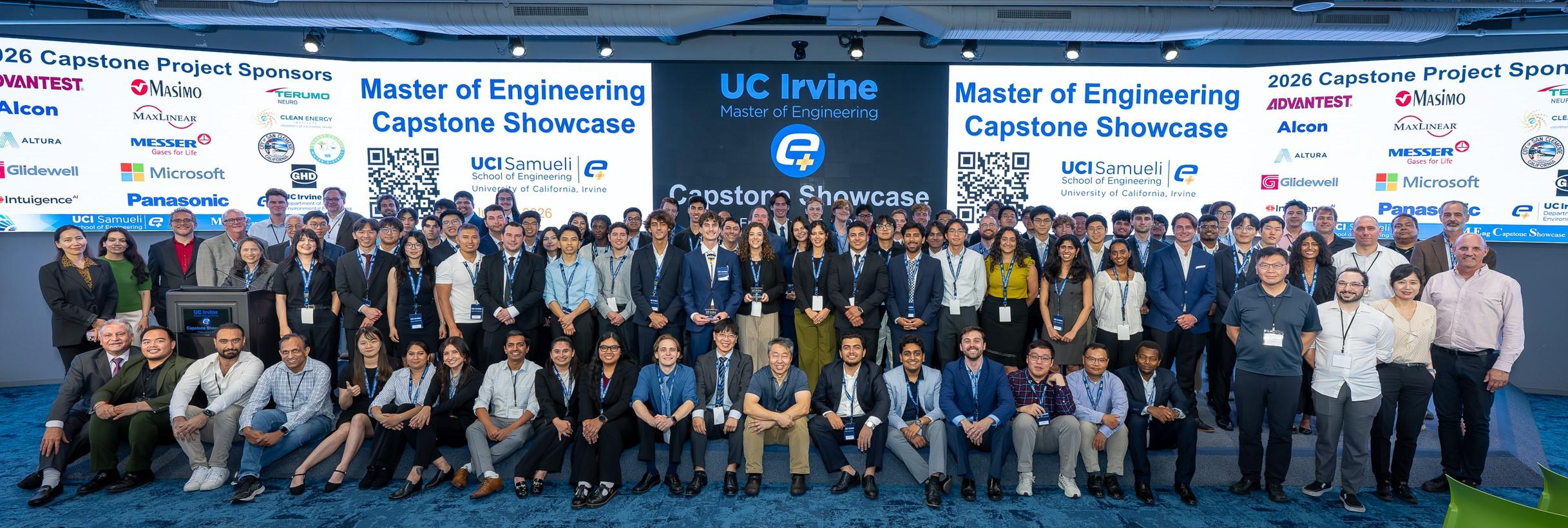 Large group photo from the 2026 UC Irvine Master of Engineering Capstone Showcase featuring graduate students, faculty, staff, and industry sponsors gathered on stage after the event. The backdrop displays the showcase title, UC Irvine Samueli School of Engineering branding, sponsor logos, and QR codes for event information.