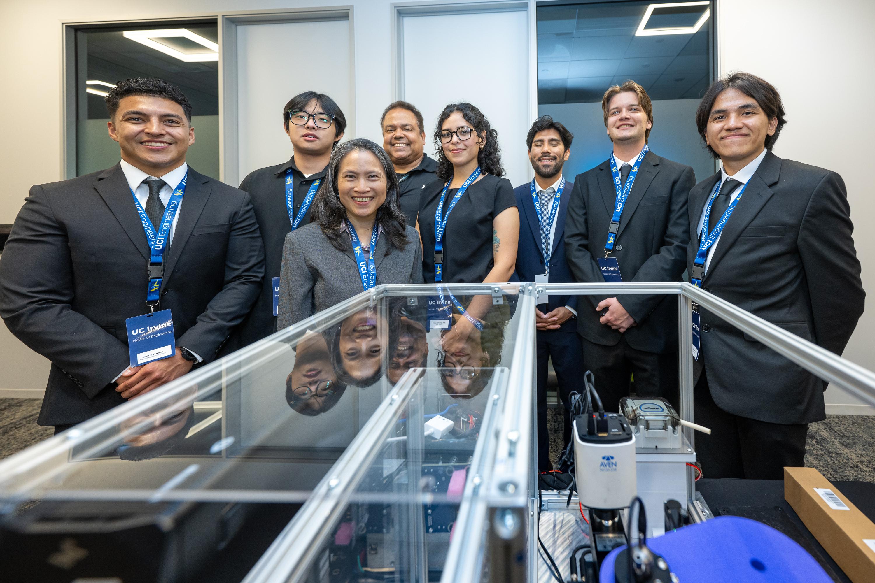 Master of Engineering capstone team posing with faculty and an industry mentor behind their engineering prototype and demonstration equipment during the UC Irvine Capstone Showcase.